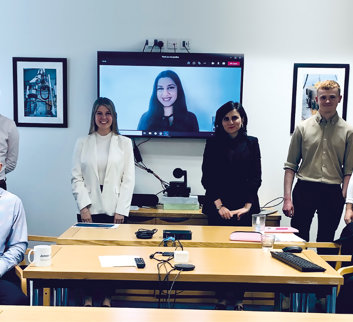 eight employees in a boardroom smiling to camera with one employee on a screen behind them